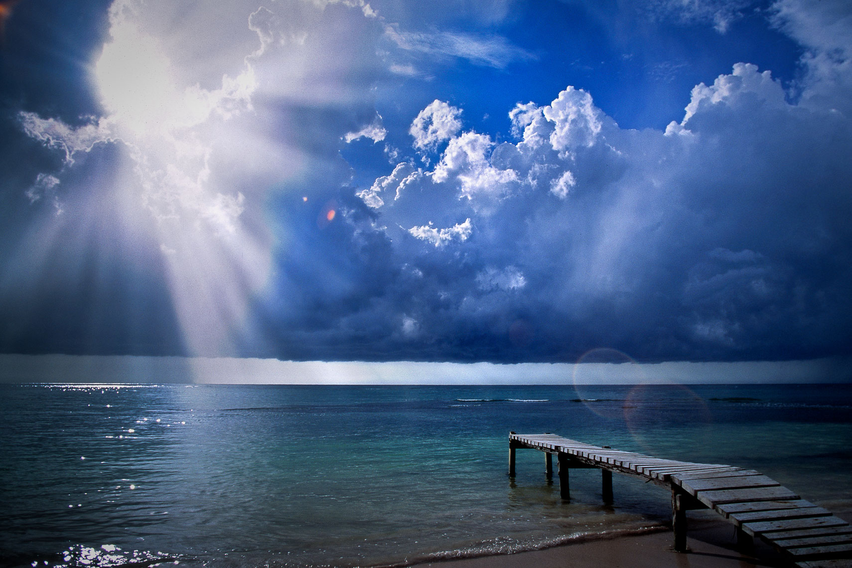 crepuscular rays over pier on beach in cuba